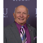  Carl Inzerillo, DO (COM 1964) smiles in a grey suit and purple tie. 